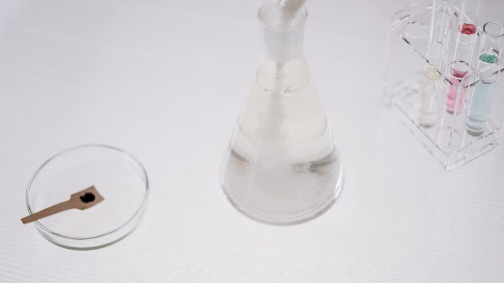 Close-up of laboratory glassware including a flask, test tubes, and petri dish on a white surface.