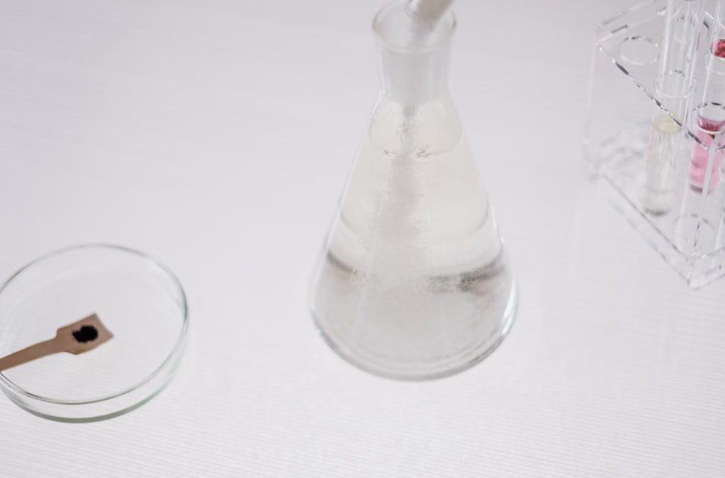 Close-up of laboratory glassware including a flask, test tubes, and petri dish on a white surface.